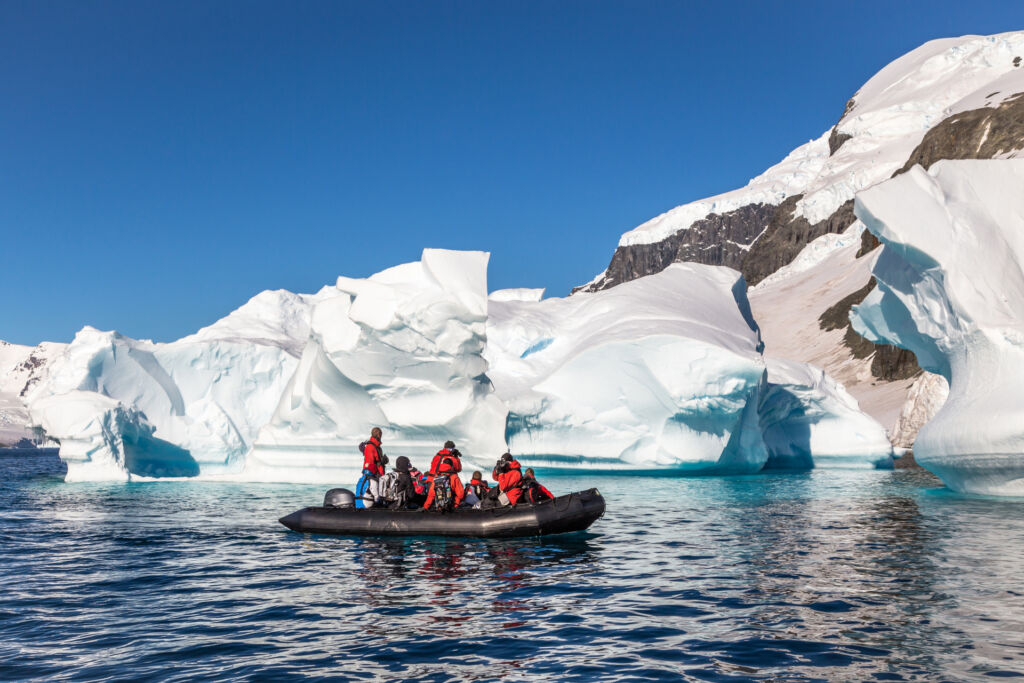 Boat full of tourists explore huge icebergs drifting in the bay near Cuverville island, Antarctic peninsula