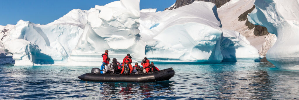 Boat full of tourists explore huge icebergs drifting in the bay near Cuverville island, Antarctic peninsula